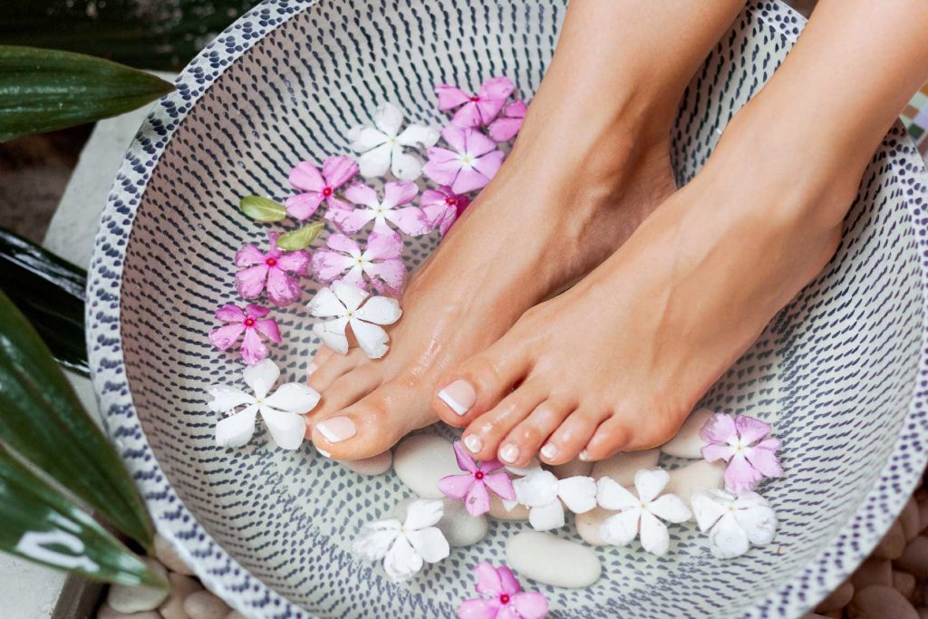 a person's feet in a bowl of water with flowers